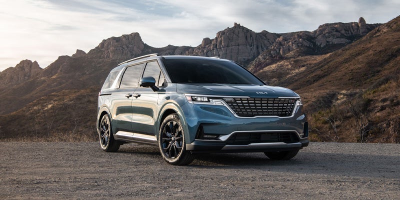 An image of a blue 2024 Kia Carnival on the roads backed by mountains. 