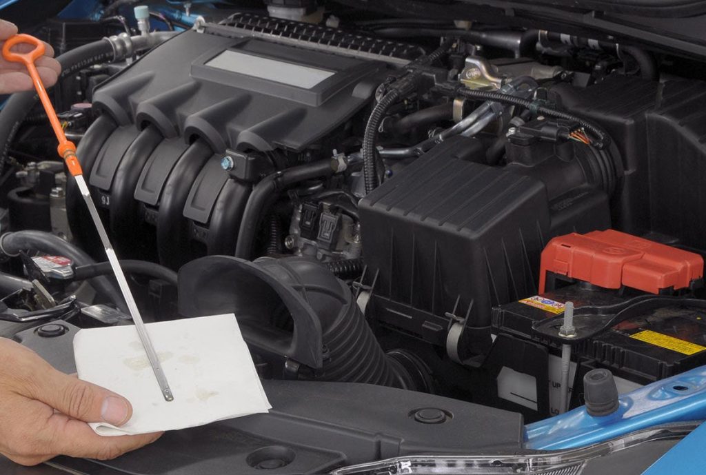 An image of an oil dipstick checking the health of a system in front of an auto engine.