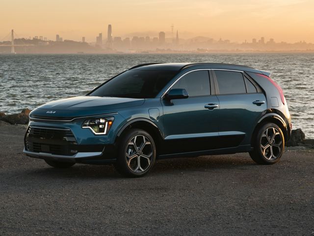 A blue Kia Niro Hybrid sitting on the shores of a beach with a city skyline in the background.