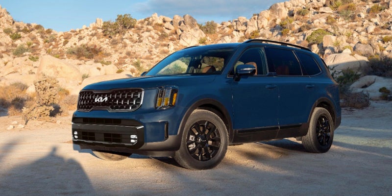 A blue Kia Telluride sitting in a parking lot in front of a sand dune.