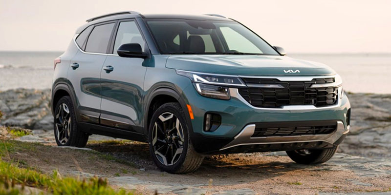 An image of a blue-green Kia Seltos sitting on a rocky plateau backed by a vast body of water.