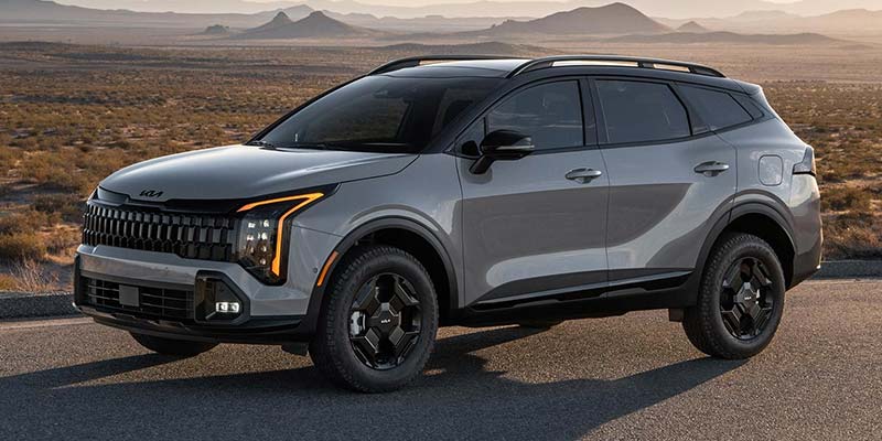 Gray Kia Sportage with black wheels parked on an asphalt road in a desert landscape.