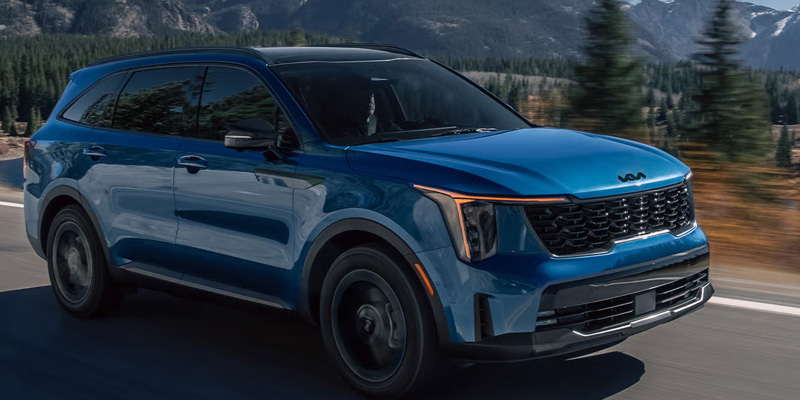Blue Kia Sorento driving on a mountain road with a forest in the background.