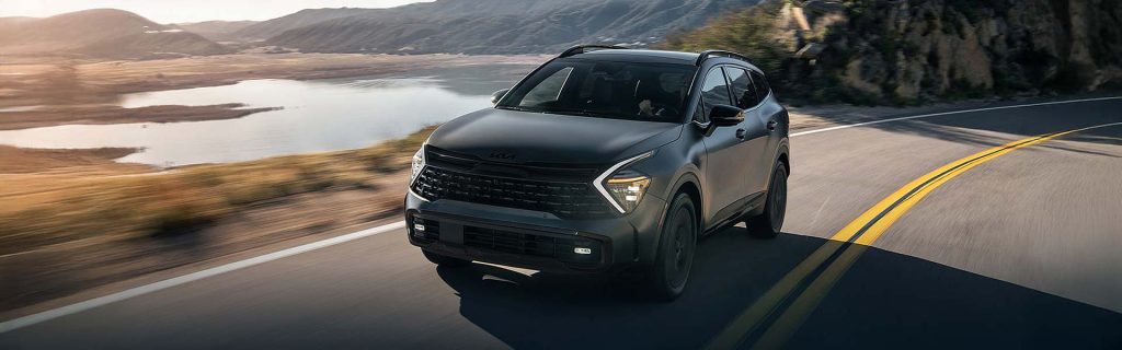 Silver Kia SUV driving along a coastal road at sunset